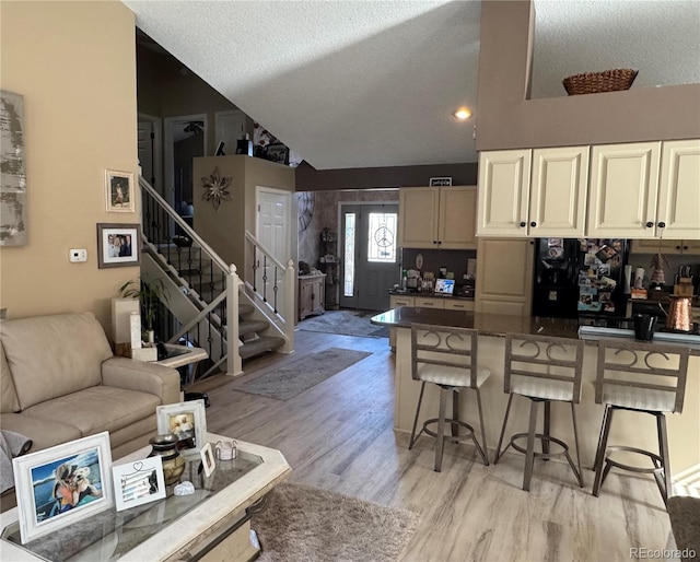 kitchen with lofted ceiling, a breakfast bar area, light wood-type flooring, and dark countertops