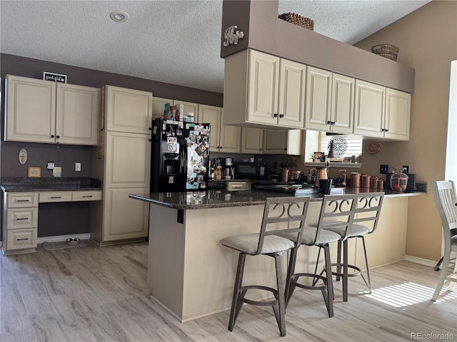 kitchen featuring a textured ceiling, light wood-style flooring, a breakfast bar, black appliances, and built in desk