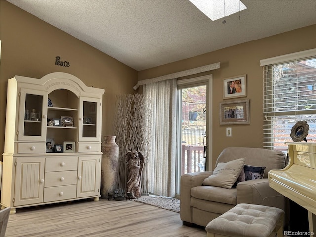 living area with light wood-type flooring, vaulted ceiling with skylight, and a textured ceiling