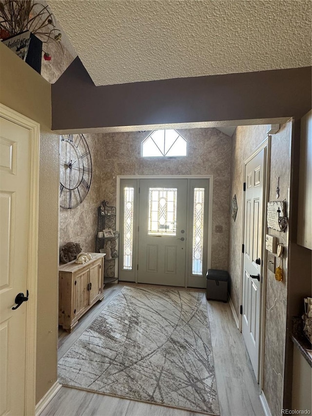 entrance foyer with lofted ceiling, light wood-style flooring, baseboards, and a textured ceiling