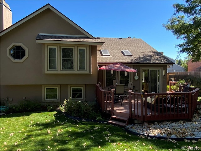 back of property featuring stucco siding, a shingled roof, a lawn, fence, and a wooden deck