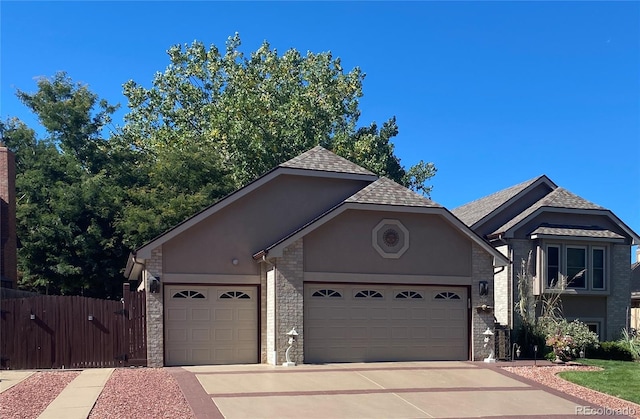 view of front of house featuring an attached garage, fence, stone siding, concrete driveway, and stucco siding