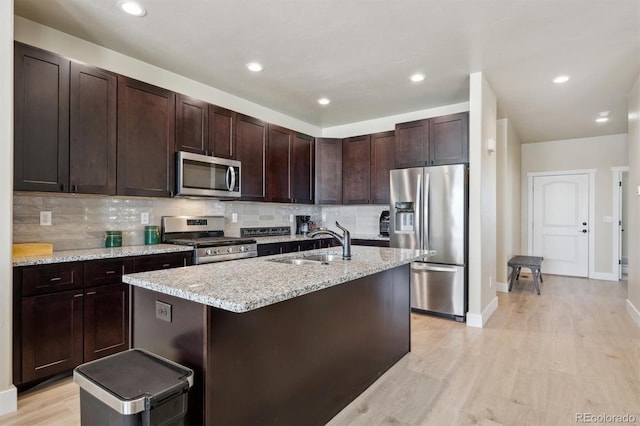 kitchen featuring a sink, stainless steel appliances, dark brown cabinets, light wood-style floors, and backsplash