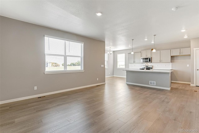 kitchen with sink, hanging light fixtures, light hardwood / wood-style flooring, decorative backsplash, and an island with sink