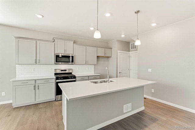 kitchen featuring pendant lighting, light wood-type flooring, stainless steel appliances, and a kitchen island with sink