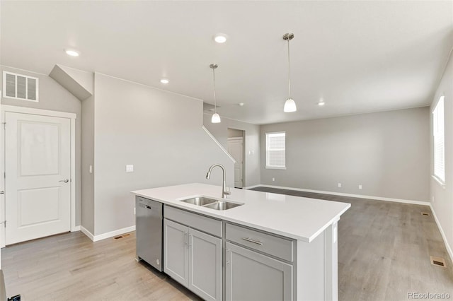 kitchen featuring a kitchen island with sink, hanging light fixtures, sink, stainless steel dishwasher, and light wood-type flooring