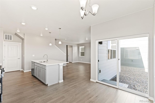 kitchen with sink, hanging light fixtures, a chandelier, wood-type flooring, and a kitchen island with sink