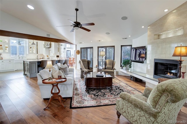 living room with a tile fireplace, light hardwood / wood-style floors, vaulted ceiling, and ceiling fan