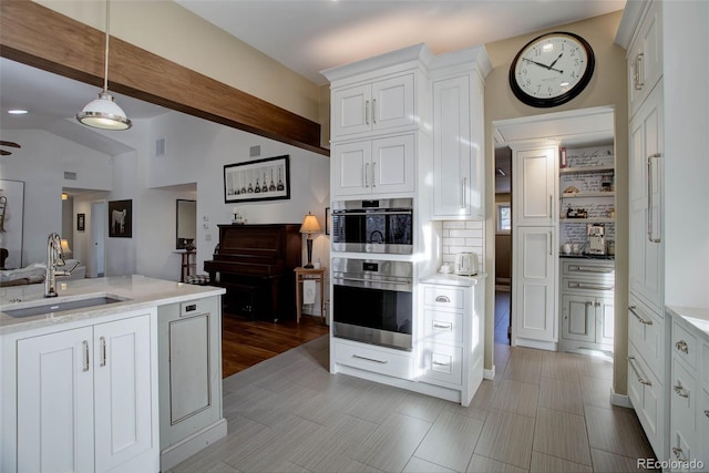 kitchen with beamed ceiling, white cabinetry, sink, and hanging light fixtures