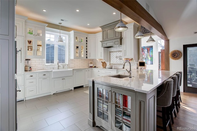 kitchen featuring light stone countertops, sink, decorative light fixtures, a breakfast bar area, and an island with sink