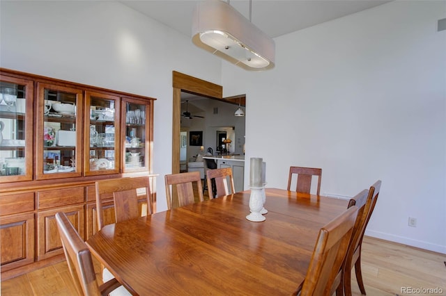 dining room with ceiling fan, light hardwood / wood-style flooring, and high vaulted ceiling