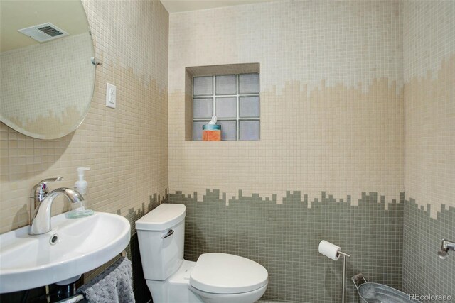 bathroom with decorative backsplash, toilet, tile walls, and sink