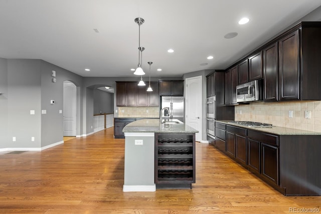 17223 W 84th Dr, Arvada, CO 80007 - kitchen featuring stainless steel appliances, arched walkways, dark brown cabinetry, recessed lighting, and wine cooler