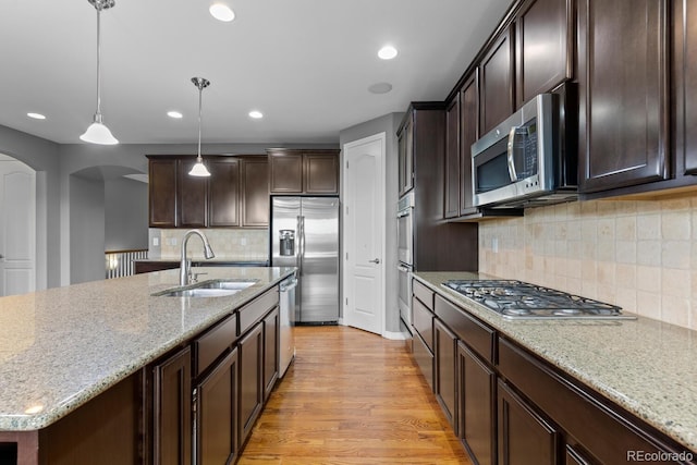 17223 W 84th Dr, Arvada, CO 80007 - kitchen with a sink, appliances with stainless steel finishes, arched walkways, dark brown cabinets, and light wood-style floors