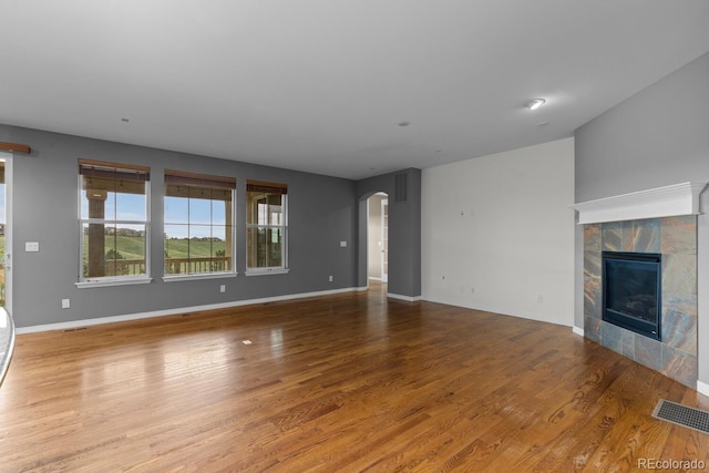 17223 W 84th Dr, Arvada, CO 80007 - unfurnished living room with arched walkways, wood finished floors, a tile fireplace, and baseboards