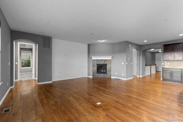 17223 W 84th Dr, Arvada, CO 80007 - unfurnished living room featuring arched walkways, light wood-style flooring, baseboards, a tiled fireplace, and recessed lighting