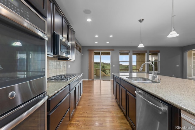 17223 W 84th Dr, Arvada, CO 80007 - kitchen with appliances with stainless steel finishes, a sink, light wood finished floors, decorative light fixtures, and decorative backsplash