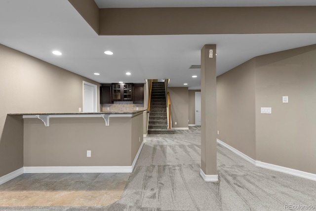 17223 W 84th Dr, Arvada, CO 80007 - kitchen featuring a breakfast bar area, stone counters, baseboards, glass insert cabinets, and dark brown cabinets