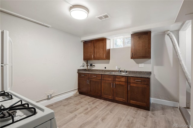 kitchen with white range with gas stovetop, a sink, light wood finished floors, dark countertops, and baseboards