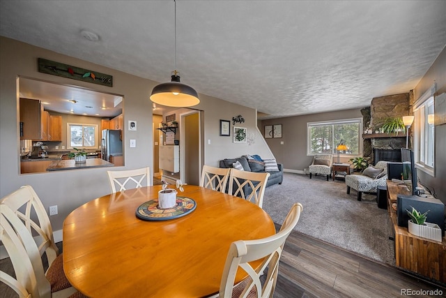 dining room featuring a textured ceiling, hardwood / wood-style floors, and a stone fireplace