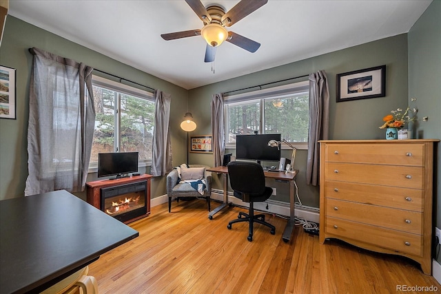 office space with a wealth of natural light, a baseboard heating unit, ceiling fan, and light wood-type flooring