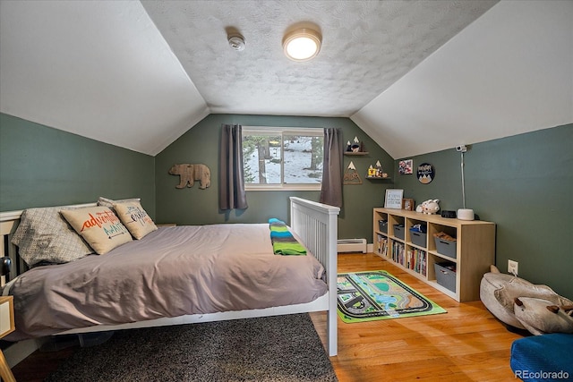 bedroom with vaulted ceiling, a textured ceiling, hardwood / wood-style floors, and a baseboard radiator