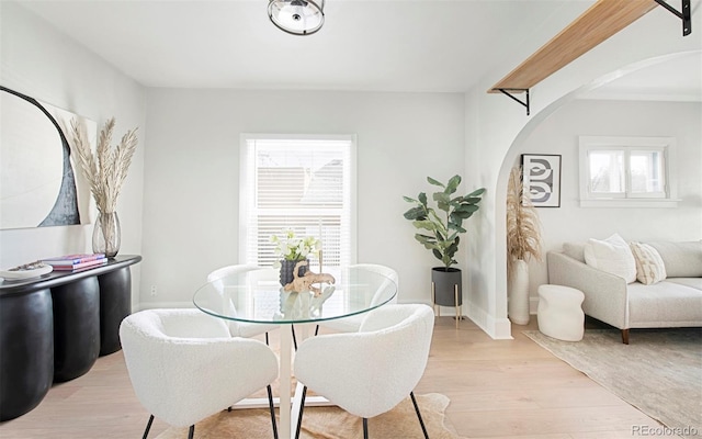 dining area featuring arched walkways, baseboards, and light wood-style flooring