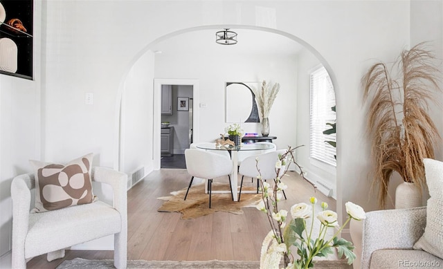 dining space featuring arched walkways, baseboards, visible vents, and wood finished floors