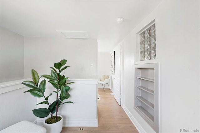 corridor featuring baseboards, built in shelves, attic access, and light wood-type flooring