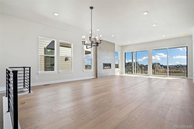 unfurnished living room featuring an inviting chandelier, a tiled fireplace, and light wood-type flooring