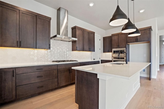 kitchen featuring pendant lighting, wall chimney range hood, sink, a kitchen island with sink, and gas cooktop