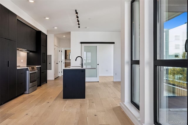 kitchen with sink, a kitchen island with sink, stainless steel range oven, and light wood-type flooring