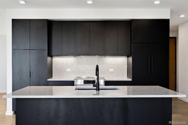 kitchen with a large island with sink, sink, backsplash, and light hardwood / wood-style floors