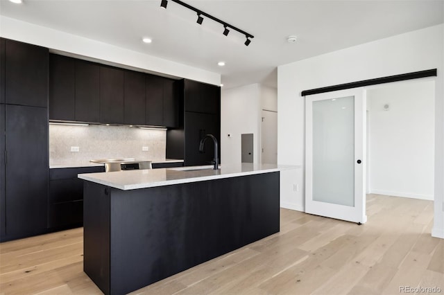 kitchen featuring a center island with sink, backsplash, a barn door, light hardwood / wood-style flooring, and sink