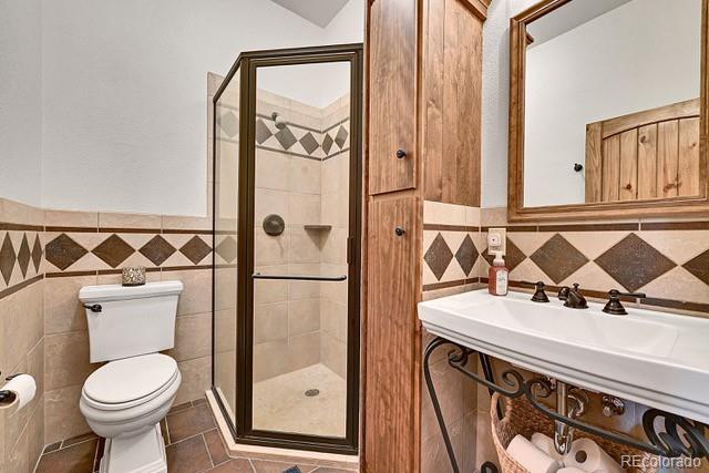 15947 Huckleberry Hts, Colorado Springs, CO 80908 - bathroom featuring tile patterned flooring, toilet, tile walls, a wainscoted wall, and a stall shower