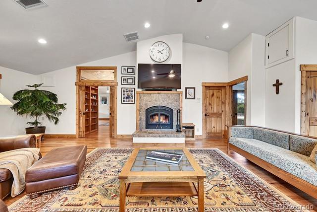 15947 Huckleberry Hts, Colorado Springs, CO 80908 - living area with a lit fireplace, visible vents, wood finished floors, and vaulted ceiling