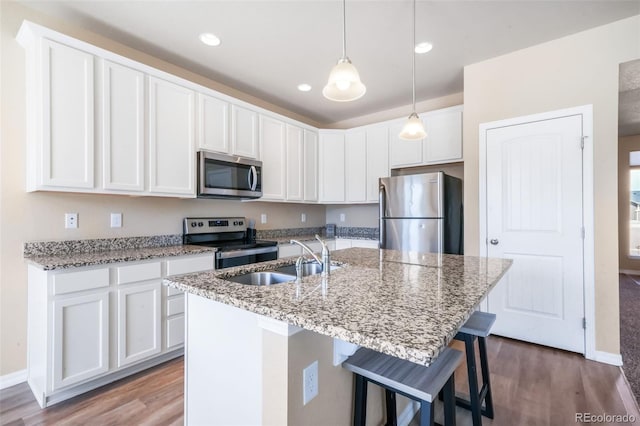 kitchen with a sink, appliances with stainless steel finishes, wood finished floors, and white cabinetry