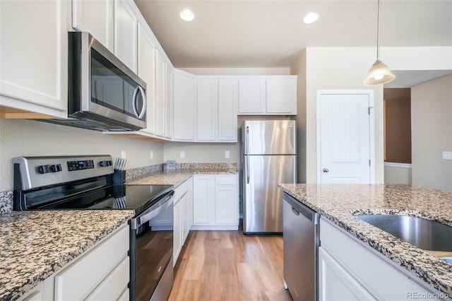 kitchen featuring white cabinets, light stone countertops, decorative light fixtures, light wood-style floors, and stainless steel appliances