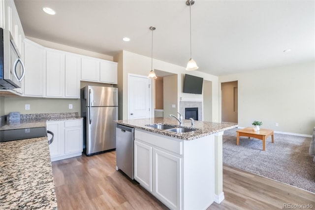 kitchen with light wood-style floors, light stone countertops, appliances with stainless steel finishes, a sink, and a center island with sink