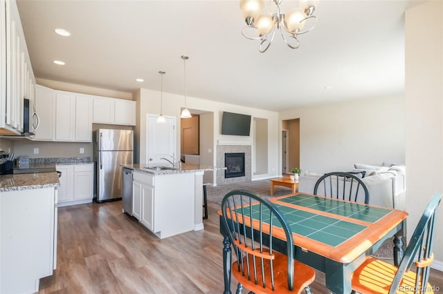 kitchen featuring white cabinets, wood finished floors, stainless steel appliances, open floor plan, and a notable chandelier