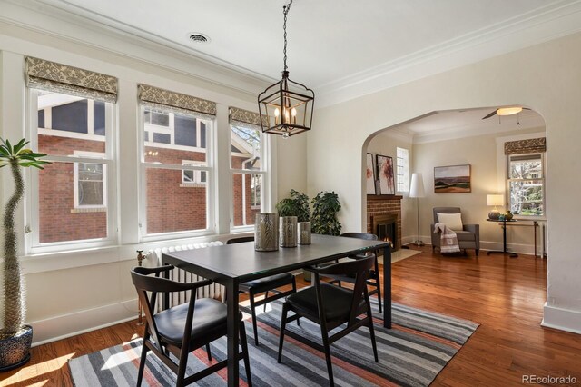 916 Adams St, Denver, CO 80206 - dining room featuring arched walkways, ornamental molding, baseboards, dark wood-style flooring, and a fireplace