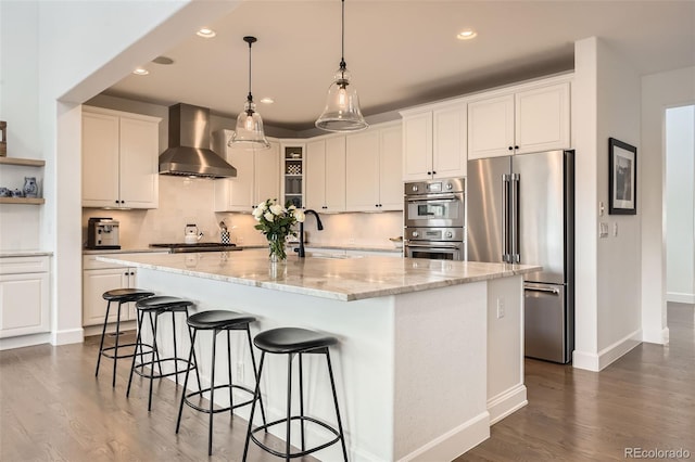 kitchen with sink, appliances with stainless steel finishes, a kitchen island with sink, white cabinetry, and wall chimney exhaust hood