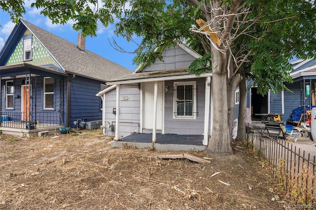 view of front of house with covered porch, a shingled roof, and fence