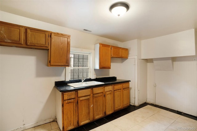 kitchen with dark tile patterned floors, a sink, visible vents, brown cabinets, and dark countertops