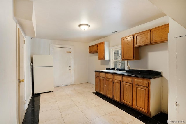 kitchen featuring a sink, visible vents, freestanding refrigerator, brown cabinets, and dark countertops