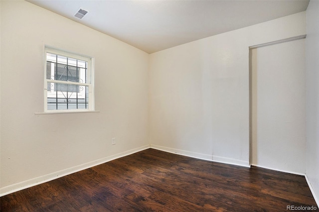 spare room with dark wood-style flooring, visible vents, and baseboards