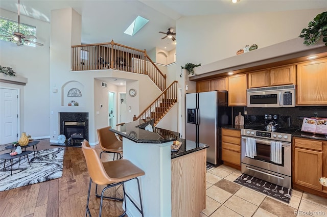 2417 S Racine Way, Aurora, CO 80014 - kitchen featuring stainless steel appliances, ceiling fan, high vaulted ceiling, a high end fireplace, and a kitchen breakfast bar
