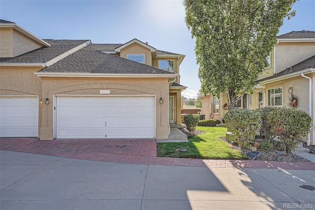 2417 S Racine Way, Aurora, CO 80014 - traditional-style home featuring roof with shingles, stucco siding, decorative driveway, an attached garage, and a front yard