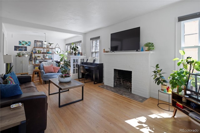 living room featuring a healthy amount of sunlight, light wood-type flooring, and a brick fireplace