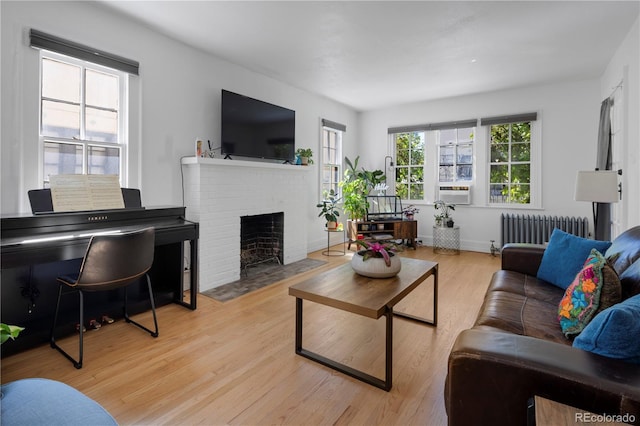 living room featuring a brick fireplace, light hardwood / wood-style flooring, and radiator